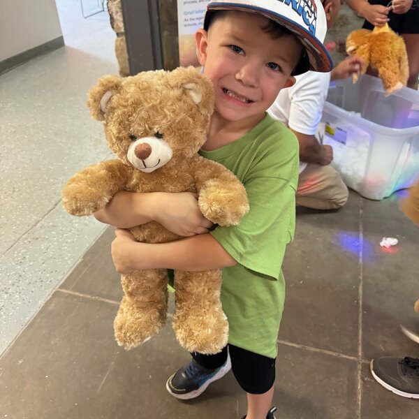 Camper poses happily with his custom Bear Hugs Workshop teddy bear during the 2026 Good Grief Camp in July.